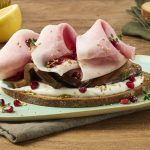 crostone di pane con tre fette di prosciutto cotto su una base di crema di yogurt in un piatto bianco su un tavolo di legno sullo sfondo