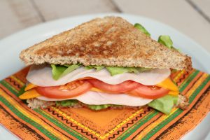 Un panino al tacchino con lattuga, pomodoro e formaggio cheddar su un toast integrale, su un tovagliolo colorato.