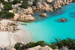 Vista dall'alto di Cala Coticcio, nell'Isola di Caprera. La sabbia bianca è lambita da acque turchesi contornate da rocce da cui spunta una macchia di vegetazione bassa.