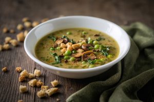 disposto su un tavolo in legno alcuni crostini, un tovagliolo verde e un piatto di zuppa si piselli e legumi.